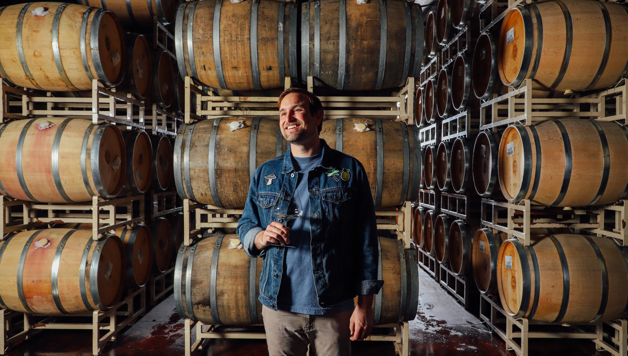 Myles Nelson holding a glass of white wine in the cellar