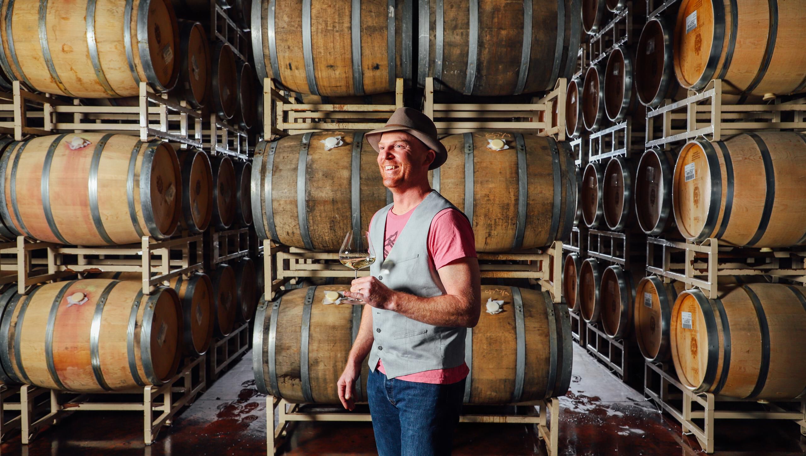 Shane Moore holding a glass of white wine in a cellar