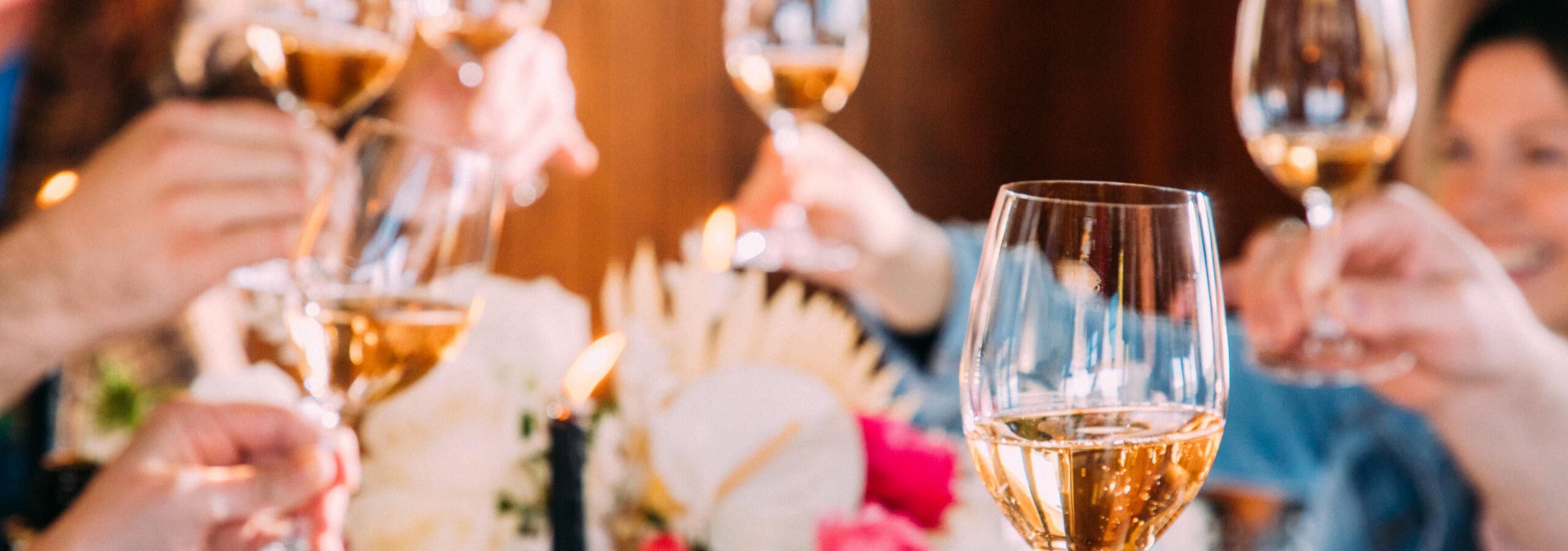 Gathering of people around a table with flowers all holding up glasses of white wine
