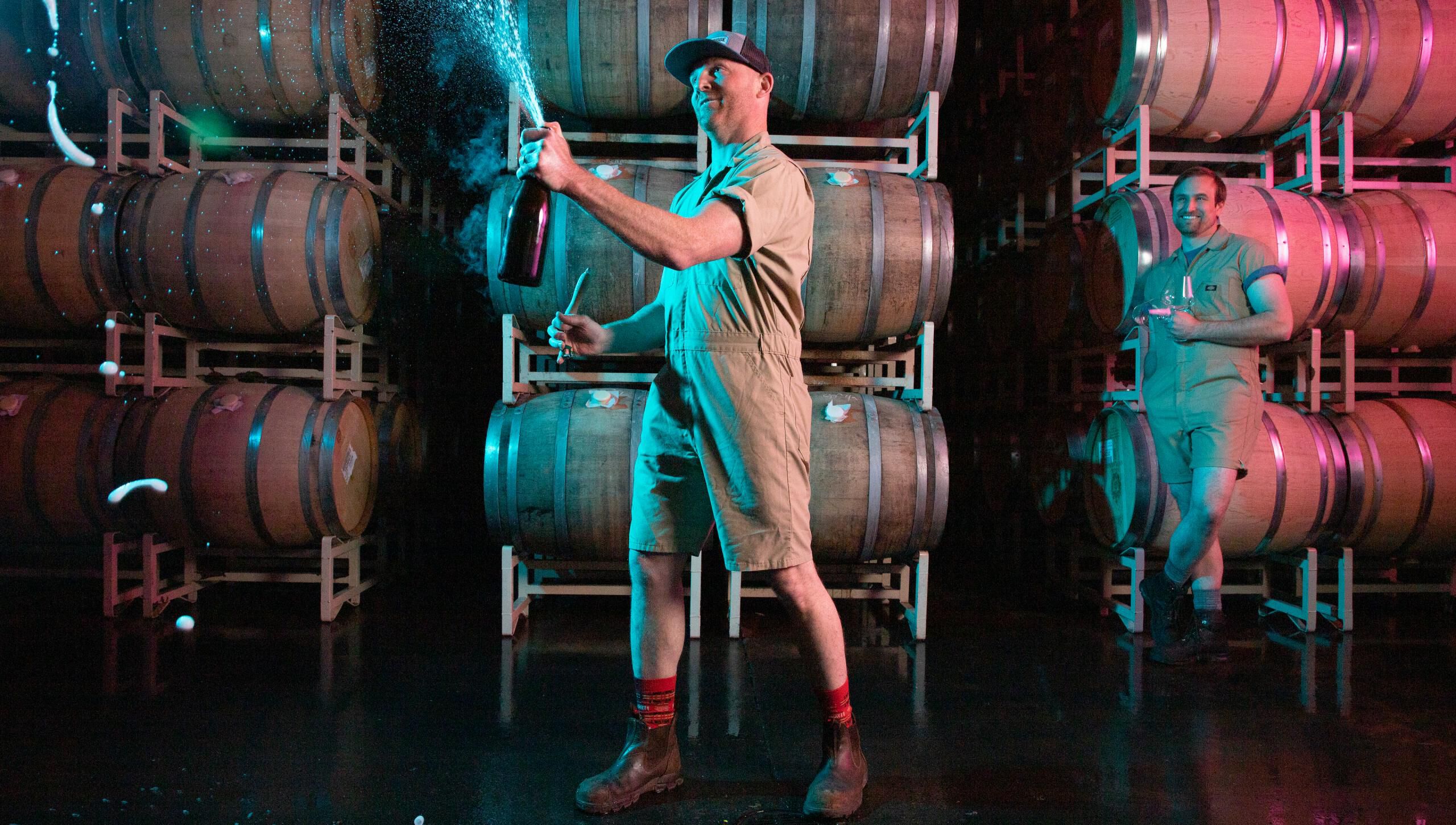 Man holding and opening a bottle of sparking wine spraying wine in the cellar