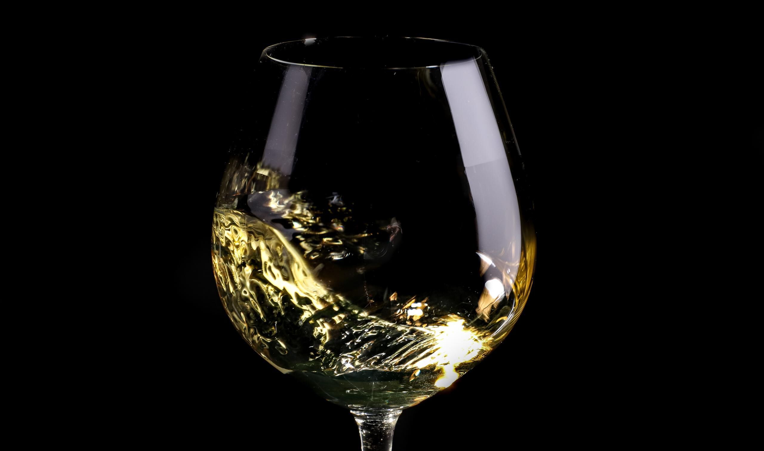 Chardonnay swirling in a glass against a black background