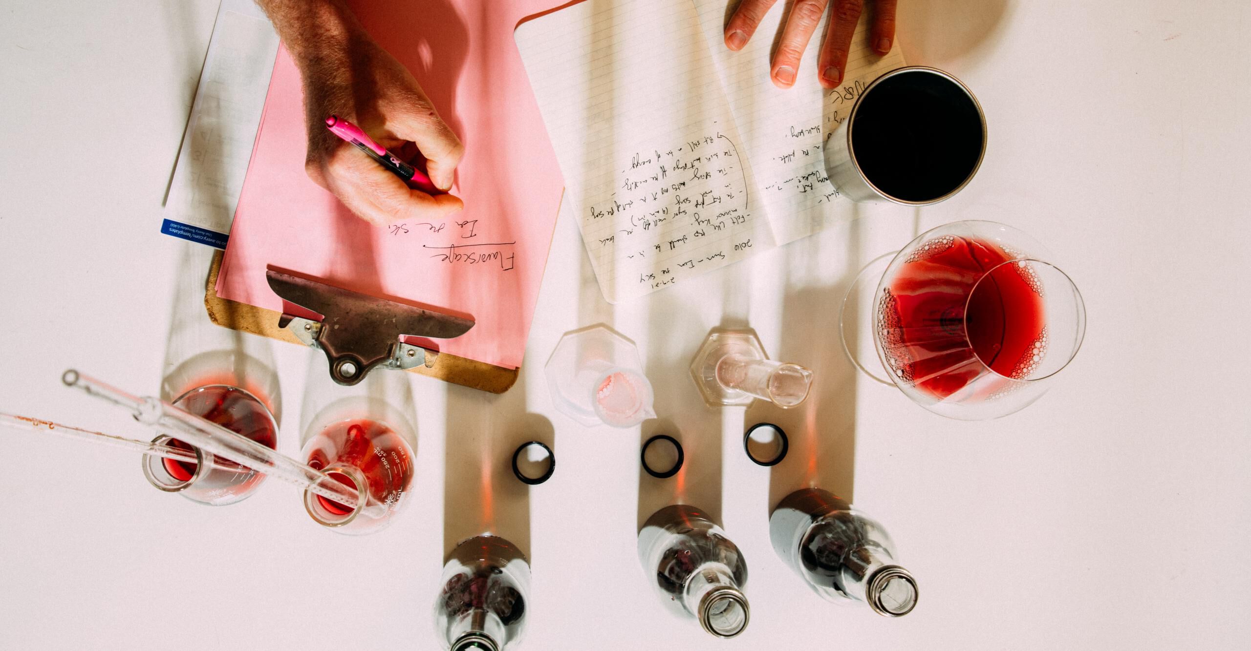 Overhead shot of a person taking lab notes with wine blending beakers around the perimeter Overhead shot of a person taking lab notes with wine blending beakers around the perimeter